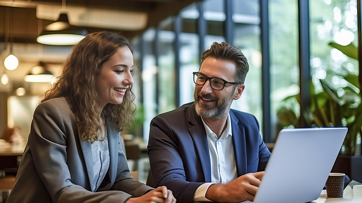 Deux professionnels souriants travaillant ensemble sur un laptop dans un espace de coworking lumineux