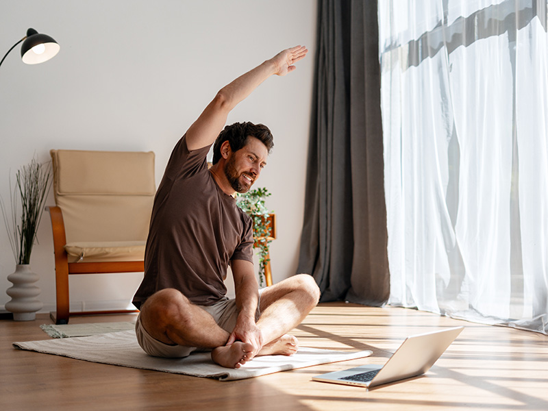 Homme souriant faisant des étirements chez lui devant son laptop — coaching sport et bien-être